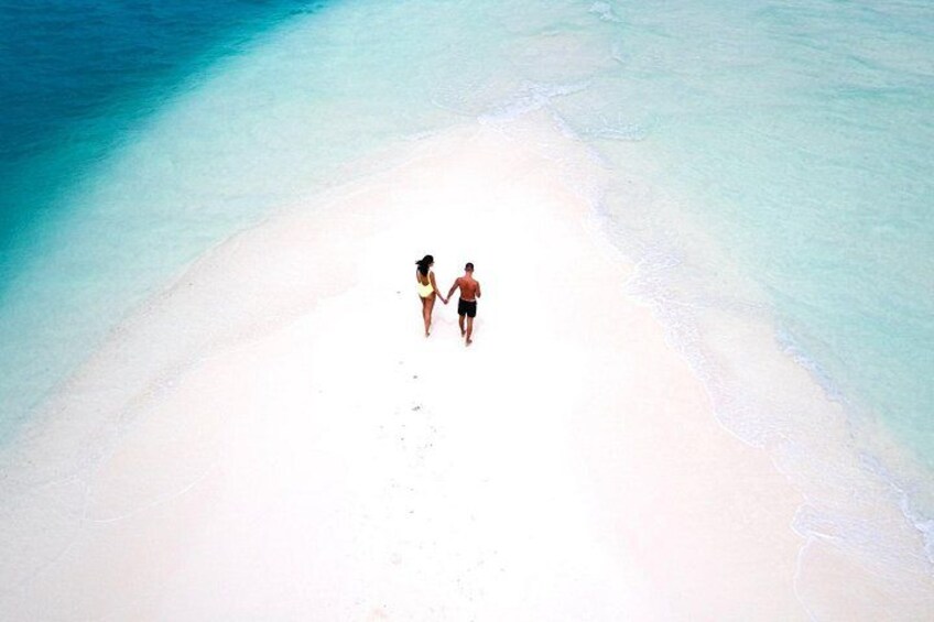 Una pareja caminando sobre una playa de arena blanca con agua turquesa cristalina. 2