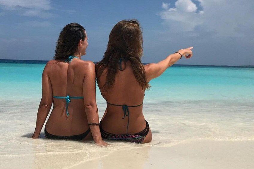 Two people sitting on a beach with turquoise water in the background. 3