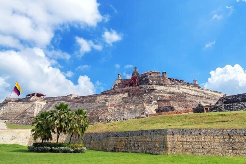 A large ancient fortress with a flag, palm trees, and a clear sky. 1