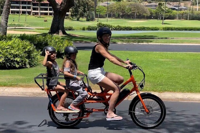 A person riding a tricycle with two children. 1
