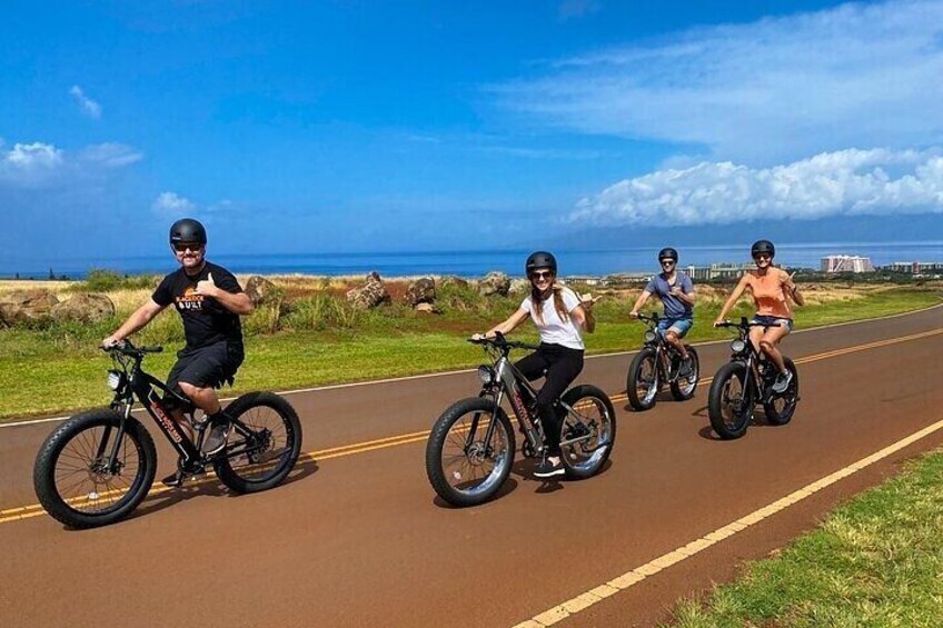 Four people riding bicycles on a paved path with a scenic ocean view. 2
