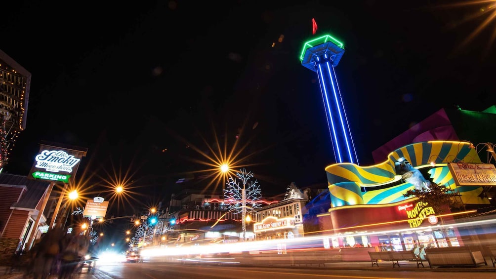 A brightly lit street at night with neon signs, a tall tower, and a colorful building. 5
