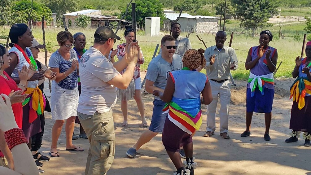 A group of people outdoors, some clapping and others watching. 1