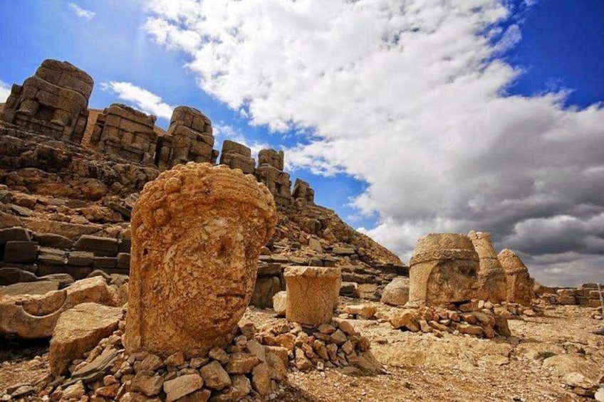 Ancient stone ruins with large, weathered columns and a rocky landscape under a partly cloudy sky. 2