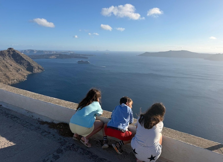 Three people sitting on a concrete ledge overlooking a coastal landscape with a clear sky. 5