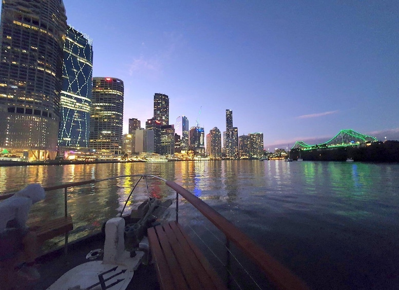 A city skyline at dusk with illuminated buildings and a bridge with green lights. 1