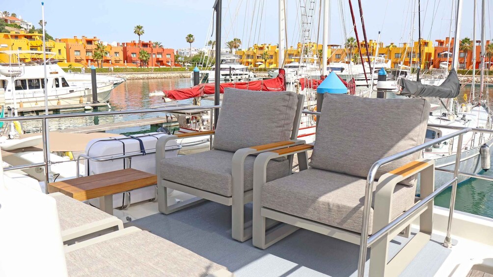 A marina with boats docked, a couple of chairs, and a building with orange and yellow facades in the background. 4