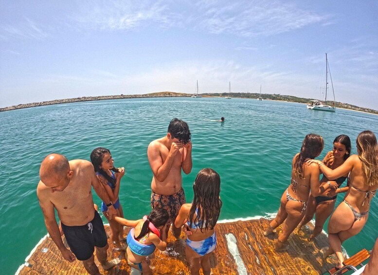 A group of people on a wooden dock by a turquoise sea with boats in the background. 3