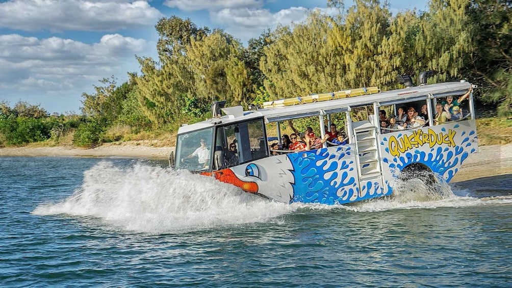A watercraft with a blue and white design, labeled 'QuackDuck,' moving through water with passengers on board. 1