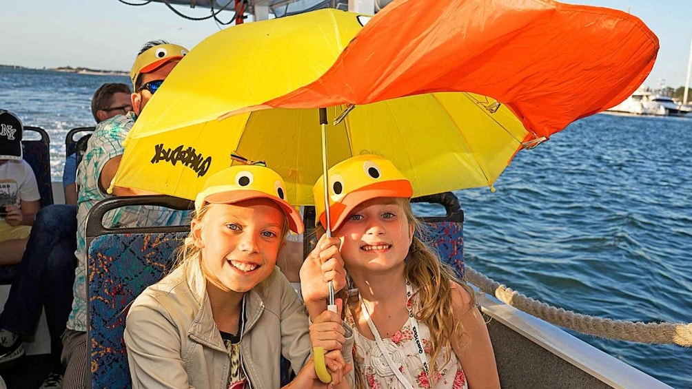 Two people on a boat holding yellow and orange umbrellas with duck faces. 3