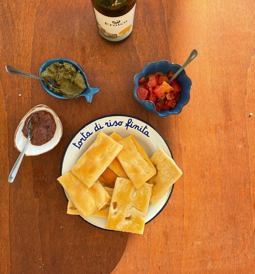 Un plato de pan plano, una botella de vino y dos recipientes pequeños con salsas sobre una mesa de madera. 2