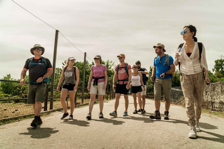 A group of people walking on a paved path with a chain-link fence and trees in the background. 3