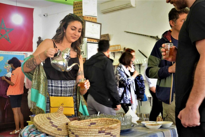 A woman pouring a drink from a metal pitcher, a table with glasses and a woven basket, and a red flag with a green star in the background. 5