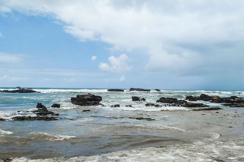 A rocky shoreline with waves crashing against the rocks under a partly cloudy sky. 4