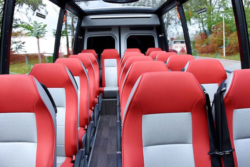 A bus interior with red and grey seats, a central aisle, and windows with a view of trees and a road. 4