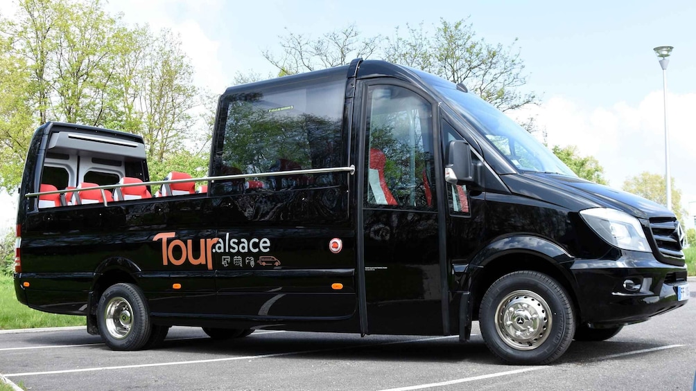 A black Touralsace tour bus parked on a road with trees in the background. 3