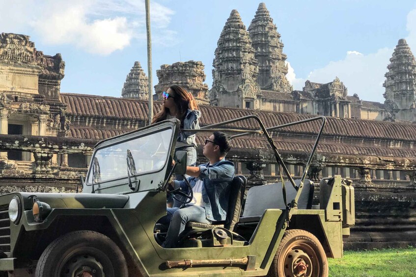 Un jeep verde con dos pasajeros, uno conduciendo y otro sentado, frente a un templo antiguo grande con múltiples torres. 1