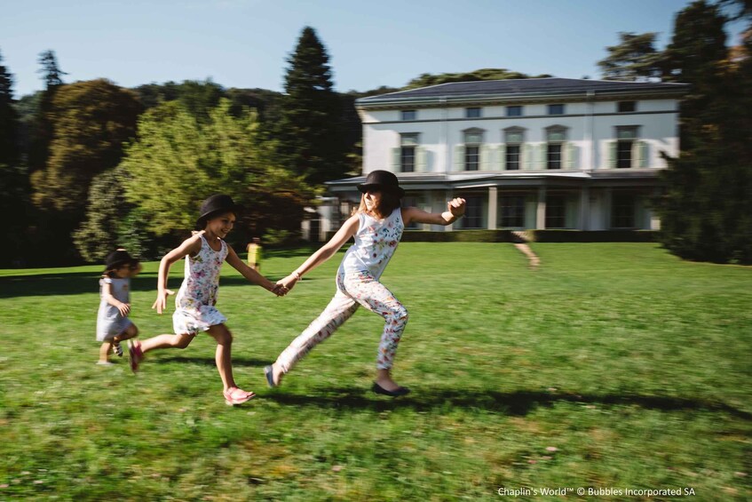 Three children running on a grassy lawn in front of a large white building with columns. 2