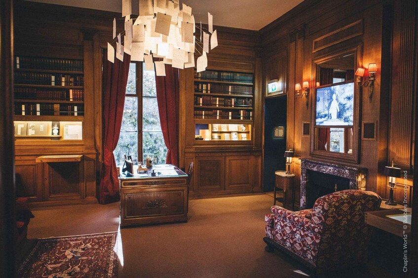 A library with bookshelves, a fireplace, a patterned armchair, and a chandelier. 3
