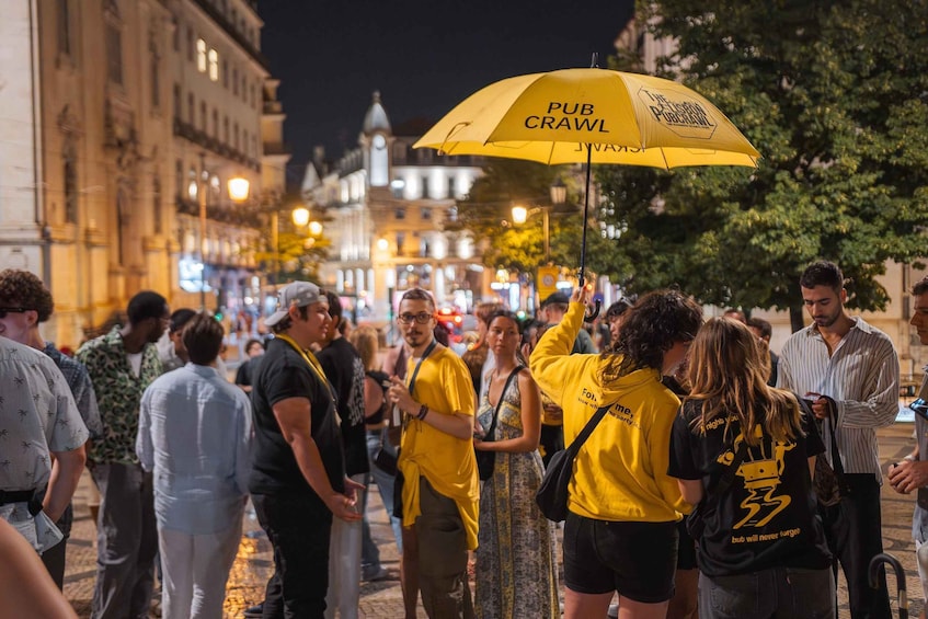A crowded street at night with people wearing yellow and black clothing, and a yellow umbrella with 'PUB CRAWL' text. 4