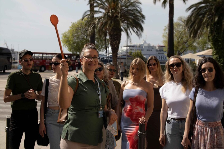 A group of people standing outdoors, palm trees, and a red bus in the background. 5