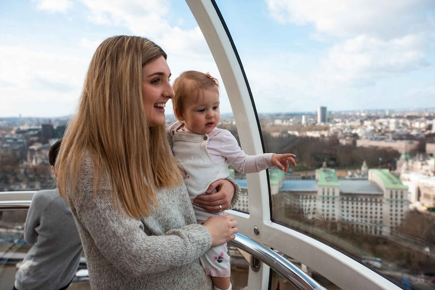 A woman holding a child on a cable car with a cityscape in the background. 5