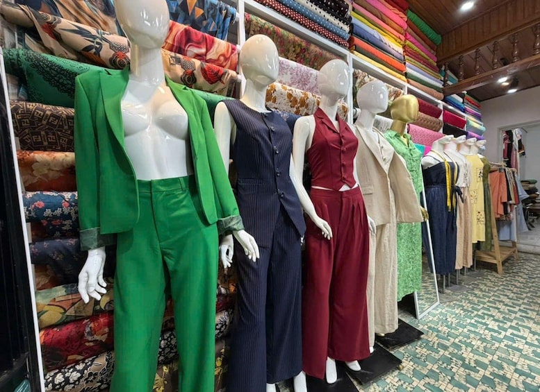 Mannequins dressed in various outfits in a clothing store with a patterned floor and shelves of folded fabrics. 2