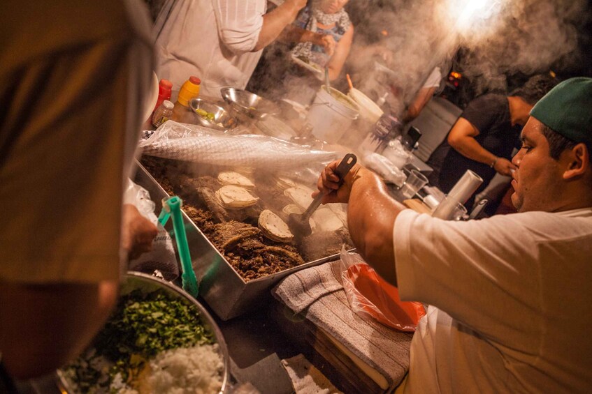 A street food vendor cooking at a stall with various ingredients and utensils visible. 2