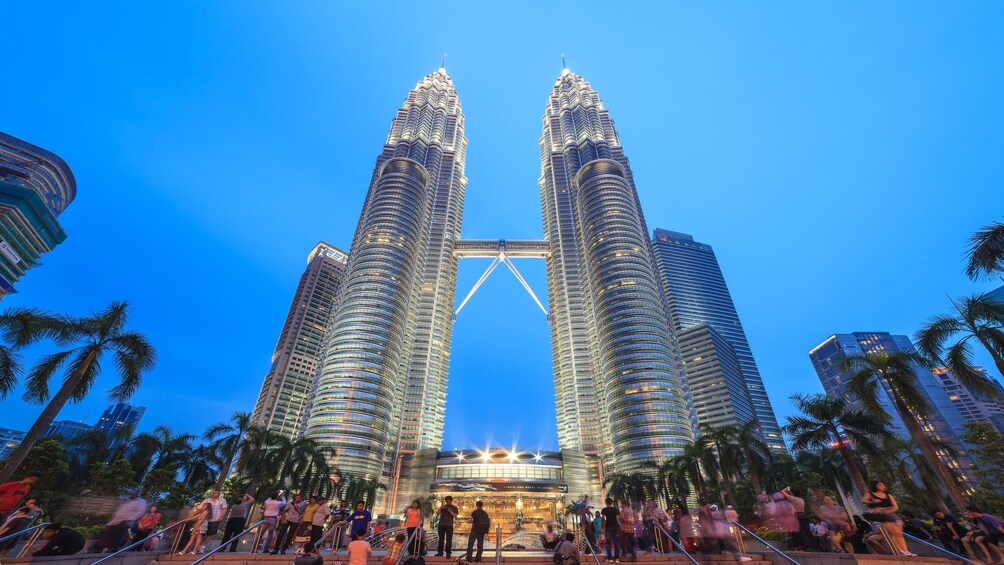 The Petronas Twin Towers with palm trees and people around. 1