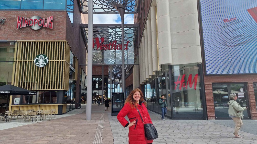 A woman in a red coat standing in front of a shopping center with stores like Kinopolis, Westfield, Starbucks, and H&M. 5