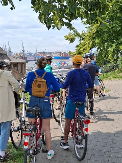 Un groupe de personnes à vélo, près d’une promenade au bord de l’eau, avec un grand cargo en arrière-plan. 2