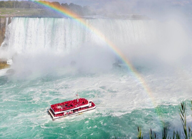 A boat with red canopies on a body of water with a waterfall in the background and a rainbow. 5