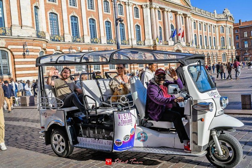 A vintage trolley with passengers, parked in front of a historic building. 1