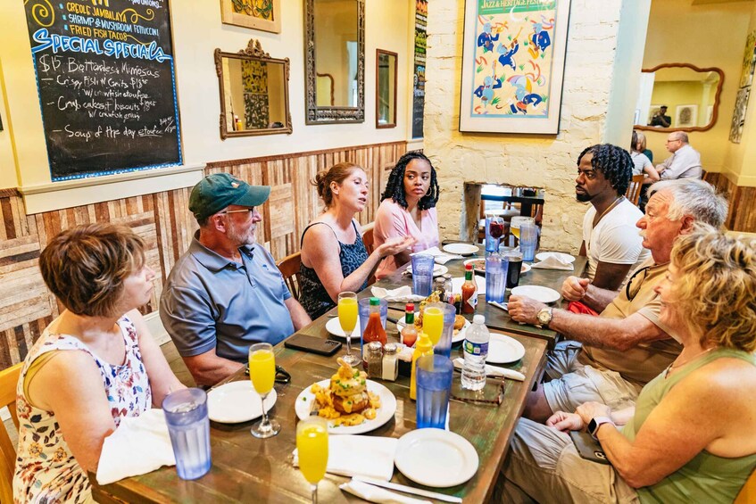 A group of people dining at a restaurant with a menu board and artwork on the wall. 1