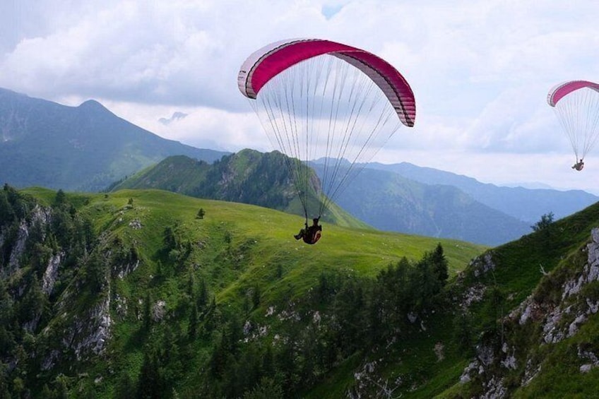 A person paragliding over a mountainous landscape with lush green hills and distant mountains under a cloudy sky. 5