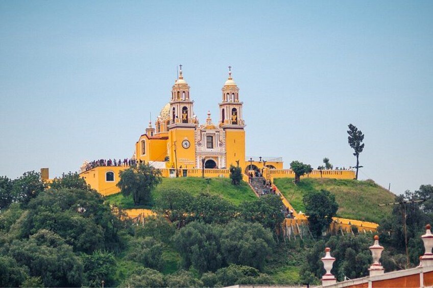 A large yellow church with two bell towers on a hill, surrounded by greenery. 5