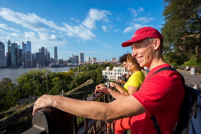 Una persona con un berretto e una camicia rossa che ammira lo skyline di una città con un fiume sullo sfondo. 1