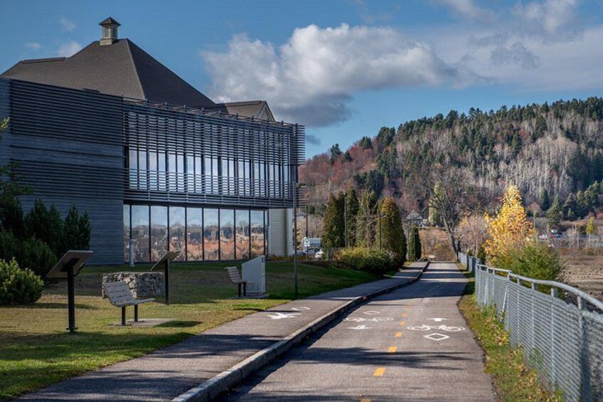 A modern building with large windows, a paved pathway, and a fenced area with trees. 2