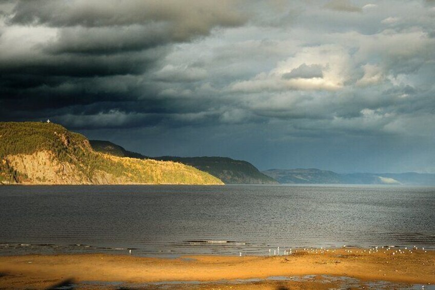 A coastal landscape with a sandy beach, calm sea, and a hill with sparse vegetation. 4