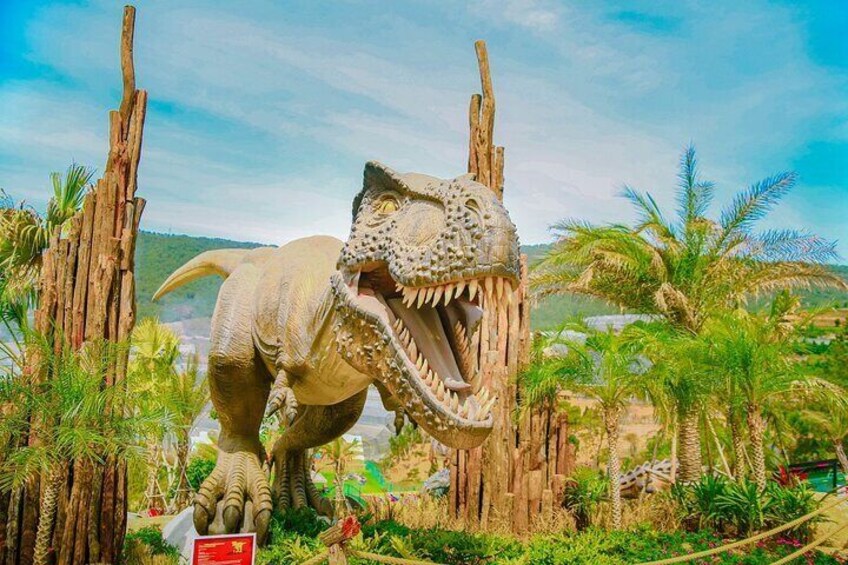 A life-sized dinosaur statue in a naturalistic setting with palm trees and wooden structures. 1