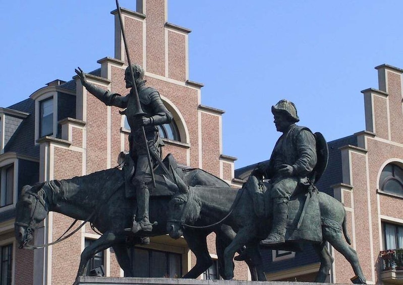 Een standbeeld van een ruiter met een lans, voor een gebouw met bakstenen muren en gebogen ramen. 1