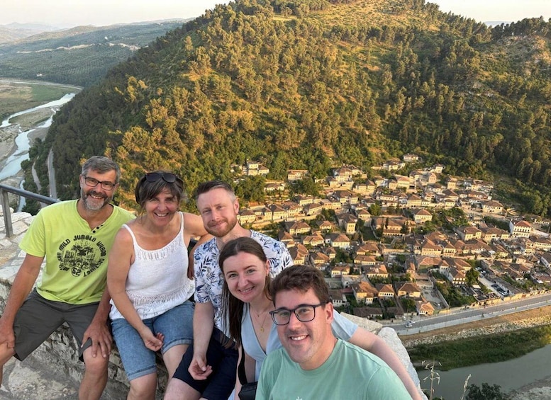 A group of people sitting on a ledge overlooking a valley with a river and a town below. 5