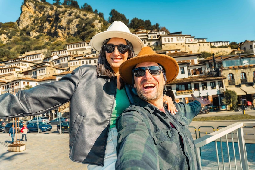 A couple taking a selfie with a mountainous backdrop and traditional buildings. 3