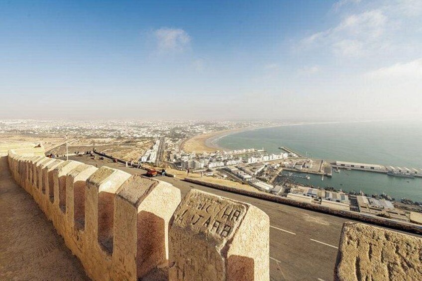 Un paisaje costero urbano con un muro marino destacado, una playa y edificios industriales. 2