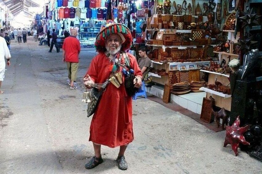 Una persona con un vestido y sombrero rojo de pie en un mercado con diversos productos a la vista. 3