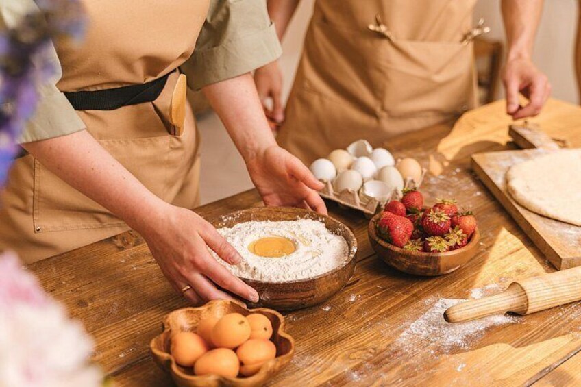 En person som lagar mat, med ingredienser som ägg, jordgubbar och mjöl på ett träbord. 1