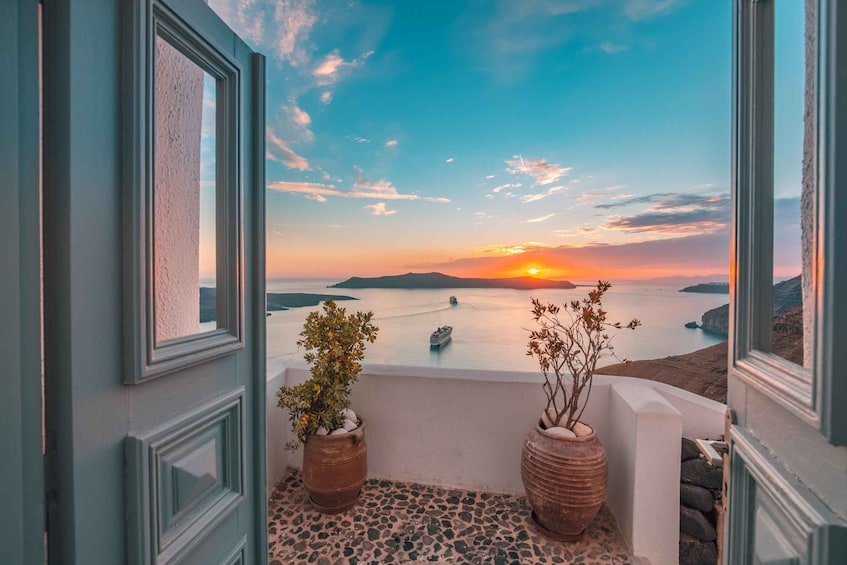 En balkon med udsigt til en solnedgang over havet, to krukkeplanter og et skib i det fjerne. 3