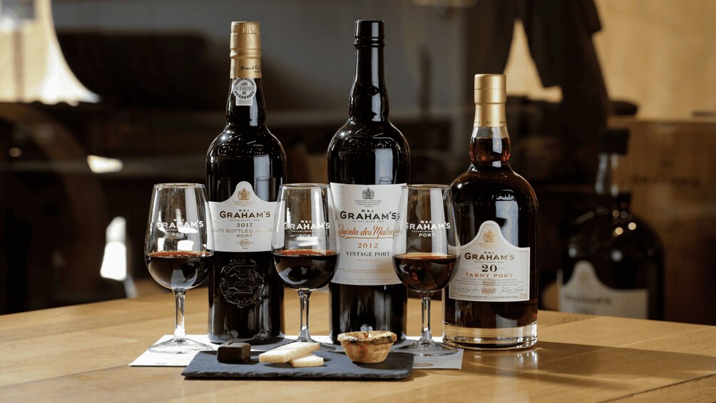 Varias botellas y copas de vino sobre una mesa, con etiquetas que señalan que son de W.J. Graham's Port. 1