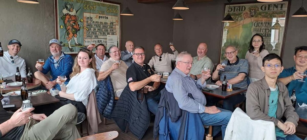 Eine Gruppe von Personen sitzt an Tischen in einem Restaurant, an den Wänden befinden sich Plakate. 5