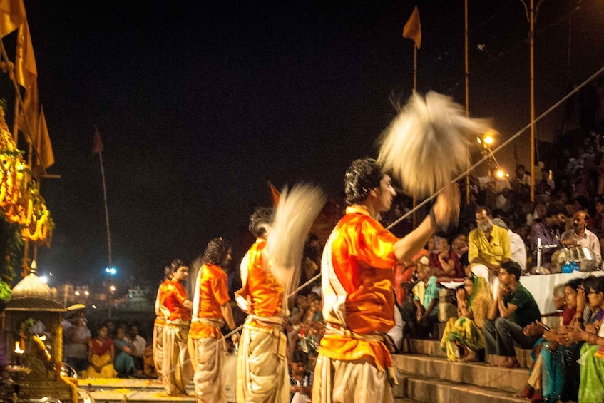 A group of performers in orange and white attire, holding white objects, performing in front of an audience. 4
